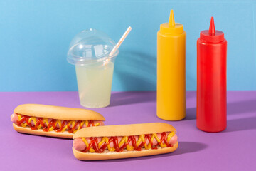 Two hotdogs, a cup of lemonade and squeeze bottles of mustard and ketchup