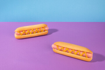 Two delicious hotdogs with mustard on violet and blue background