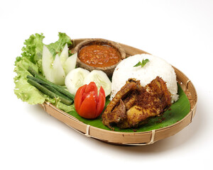 Fried chicken with ripe golden skin laid out on a wooden sheet on a white background, plus white rice, chili sauce and various vegetables, view from above. commonly used for menus and picture packs.