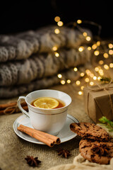 A cup of lemon tea with selective focus on the table with cinnamon, gift box and garland.