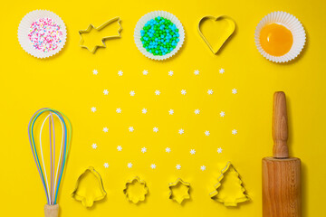 Ingredients, sugar decoration, and kitchen tools for baking on the yellow background. Cookie cutters, a rolling pin, an egg whisk. Yolk, sugar, baking decoration in muffin forms. Copy space. Top view.