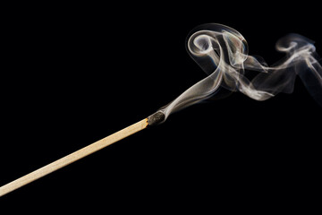 A single extinguished match with smoke rising up, isolated on a black background.