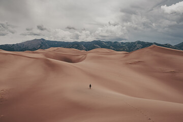 Fototapeta na wymiar A man hiking the giant sand dunes during stormy weather at Great Sand Dunes National Park in Colorado, USA