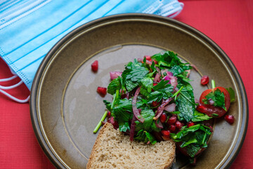 Salad of parsley, mint, pomegranate, red onion, tomato, and olive oil. Red background, disposable masks. Patient nutrition.