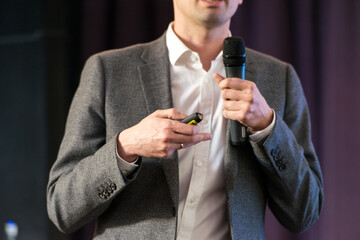 Business and speech topic: Man in a gray suit holding a black microphone a on a dark violet background