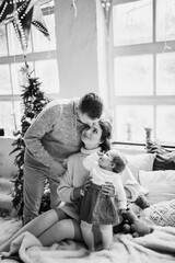 Young family with little daughter near the Christmas tree at home, caring husband hug beautiful wife, loving mother hold cute toddler in arms, smiling, winter holidays concept