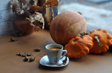 A cup of coffee, dry oak leaves and acorns, pumpkins on the windowsill. Old wooden window.