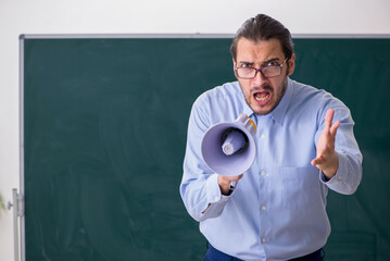 Young male teacher in the classroom holding megaphone