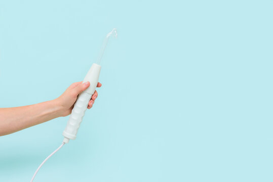 darsonval with a face nozzle in a woman's hand on a pink background. hardware skin correction, Spa care at home