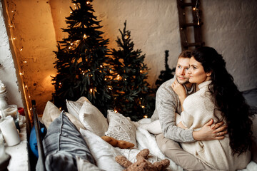Adorable couple sit near the Christmas tree at home, cuddling, romantic husband with lovely wife spend winter holidays together, enjoy happy moments, New Year celebration concept