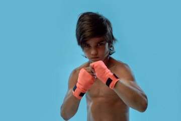 Portrait of little boy boxer with boxing bandage on hands, looking at camera ready to fight while...