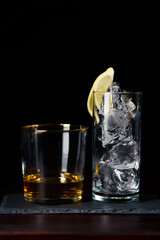 Whiskey neat and glass of ice served on slate plate. Dark red wooden table, high resolution