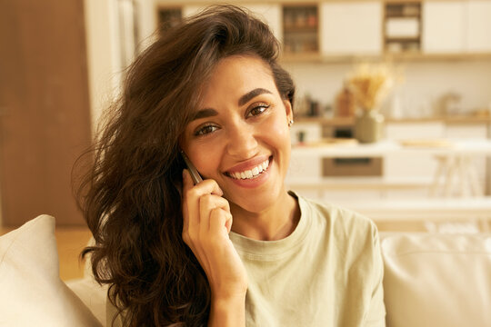 Close up image of pretty Hispanic girl enjoying nice phone conversation with boyfriend, smiling broadly at camera. Cheerful attractive young woman making calls. Electronic gadgets and devices