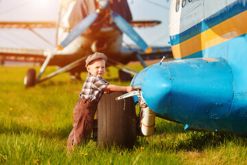 A small child stands near an old sightseeing plane and waits for his father a mechanic