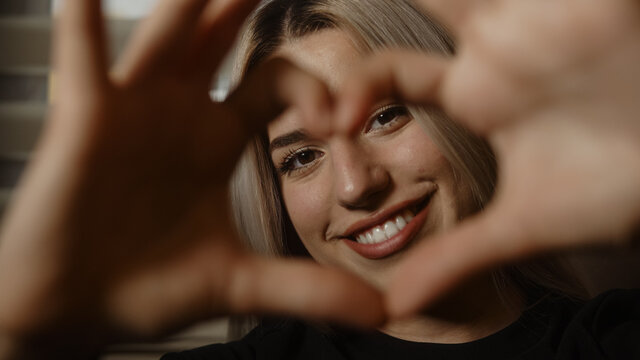 Happy smiling beautiful blonde woman, showing hands sign heart shape looking at camera, healthy and lifestyle concept