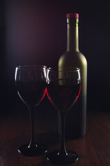 Two glasses of red wine, a bottle on a wooden table.