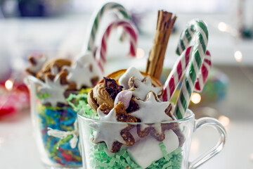 Christmas homemade sweet gifts. Christmas composition of transparent mug with cookies. Handmade home gift idea mugs with sweets, cookies, nuts, lollipops cane and New Year decorations on a light table