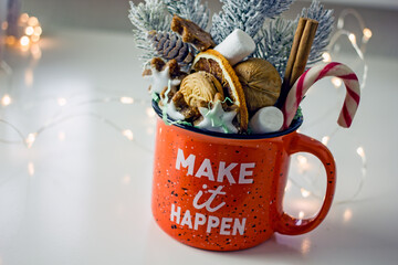 Christmas composition with homemade sweet gifts. Large orange mug with homemade cookies, nuts, sweets, candy cane and Christmas tree branch on a light table. Conception of delicious homemade gifts