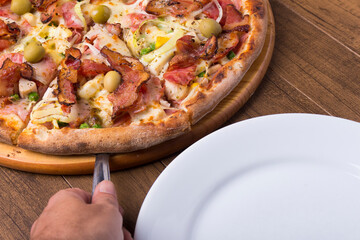Portuguese pizza made with ham, pea egg, heart of palm, pepperoni, onion and mozzarella and bacon. Serving slice of pizza with spatula. Gastronomic photography of restaurants and pizzerias.