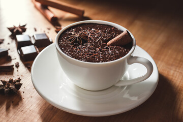 Hot chocolate drink in white cup, broken chocolate, cinnamon stick and star anise on a wooden table