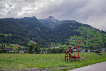 an old part from a tractor stands in a field near the mountains