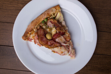 Pizza slice served on the plate. Portuguese pizza made with ham, pea egg, heart of palm, pepperoni, onion and mozzarella and bacon.
