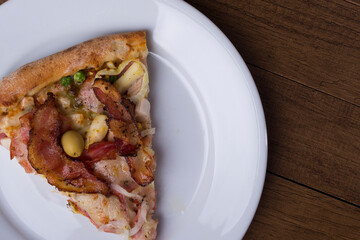 Pizza slice served on the plate. Portuguese pizza made with ham, pea egg, heart of palm, pepperoni, onion and mozzarella and bacon. Top close-up photograph. Space for texts on the right.