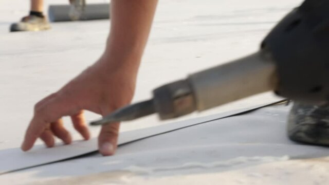 Roofer use hot air gun to weld synthetic PVC membrane.