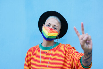 Cheerful hipster girl wearing protective face mask and doing peace gesture with hand