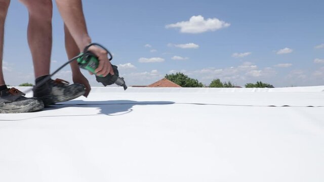 Roofer use hot air gun to weld synthetic PVC membrane.