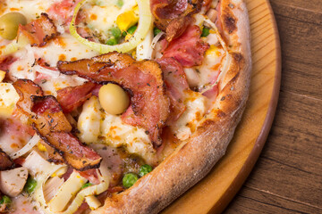 Portuguese pizza made with ham, pea egg, heart of palm, pepperoni, onion and mozzarella and bacon. Served on a wooden board. Gourmet close-up photography.