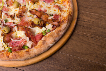 Portuguese pizza made with ham, pea egg, heart of palm, pepperoni, onion and mozzarella and bacon. Served on a wooden board. Close-up photo with space for text on the right.