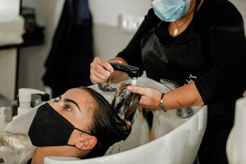 Obraz na płótnie Canvas Woman with face mask getting a fresh style at a hair salon. Woman getting a hair wash. Hairdressing concept.