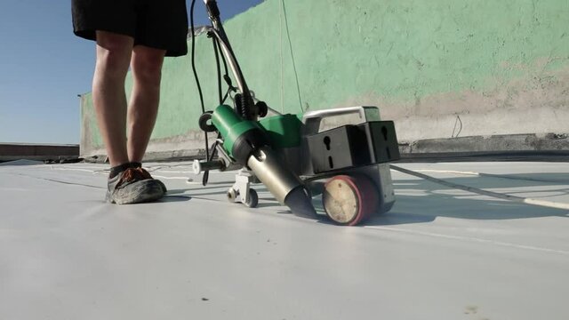 Roofer use welding machine for synthetic membrane on flat roof structure.