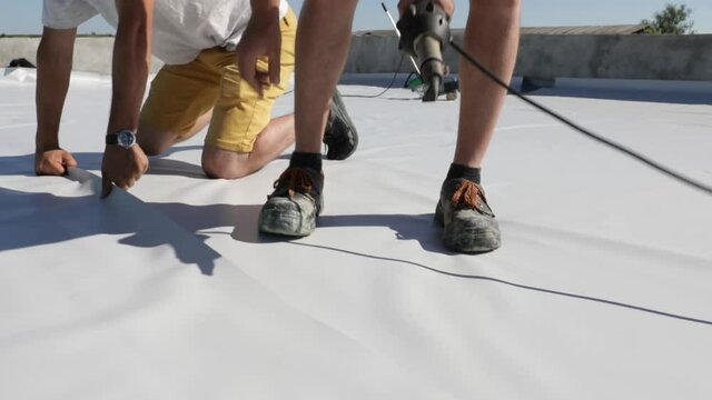 Roofer use hot air gun to weld synthetic PVC membrane.