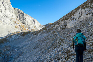 Fototapeta premium A woman hiking in Hochschwab region in Austrian Alps. Steep mountain chain in front of her. Massive Alps. Autumn vibes in the mountains. Idyllic landscape. Freedom and wilderness