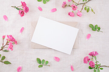 Flyer mockup, mock-up of blank greeting card on the envelope with flowers of pink roses and petals on linen napkin. Wedding, birthday  stationery. Top view.