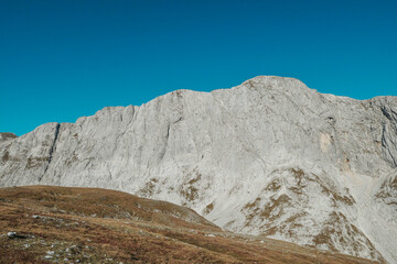 A panoramic view on the plain on top of a mountain in Hochschwab region in Austrian Alps. The flora overgrowing the slopes is turning golden. Autumn vibes. Many mountain chains in the back. Wilderness