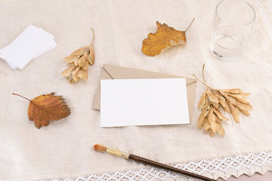 A business card on an envelope, a letter or an invitation against the background of a light linen napkin with fallen leaves. Wedding stationery mockup, advertisement or greeting card. Top view