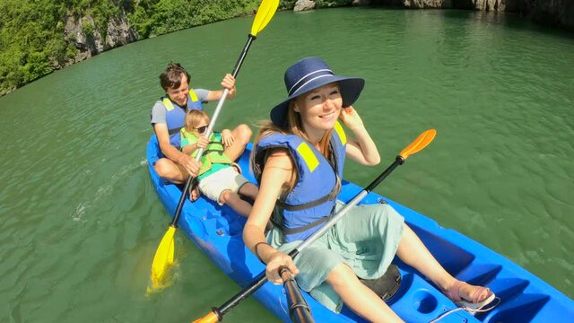 Slowmotion shot of a happy family of tourists kayaking among limestone cliffs in a Halong Bay national park, Vietnam. Travell to Vietnam concept