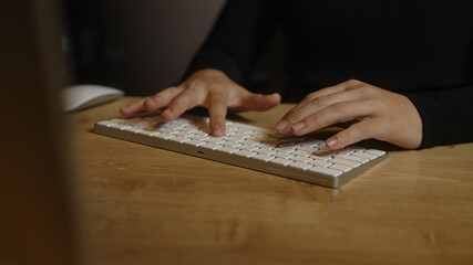 Fototapeta premium Close-up of female hands typing on a white keyboard on the table