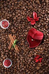 Coffee beans on a coffee beans background with red box with wedding ring, red flowers , red chocolate and cinnamon. Morning espresso. Coffee mug.	