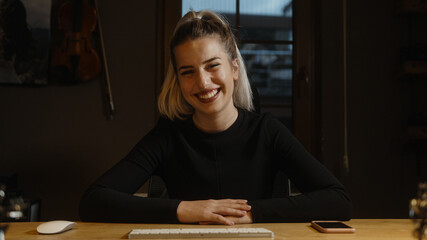 Beautiful young happy blonde business woman at the desk, hands on the table, having video talk on web camera