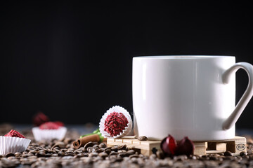 White cup full of coffee beans , red flowers and red chocolate candy against the black background. Morning espresso. Coffee mug.	