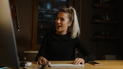 Young blond beautiful woman dressed in black spends time on the computer at the desk in the office, Office worker concept
