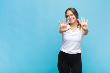 young hispanic woman smiling and looking friendly, showing number nine or ninth with hand forward,...