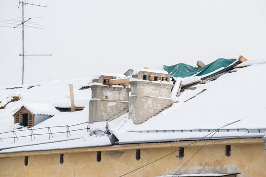 Roof Repairs Of An Apartment Building.  The Roof Collapsed Under The Weight Of Snow. Damaged Falling Roof And Chimney On Sunny Day With Clear Blue Sky.