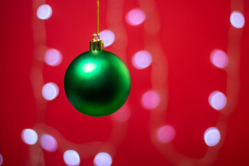 Fototapeta na wymiar Green Christmas ball on a background of a glowing garland. Christmas decorations on a red background. Holiday decorations. Christmas concept. 