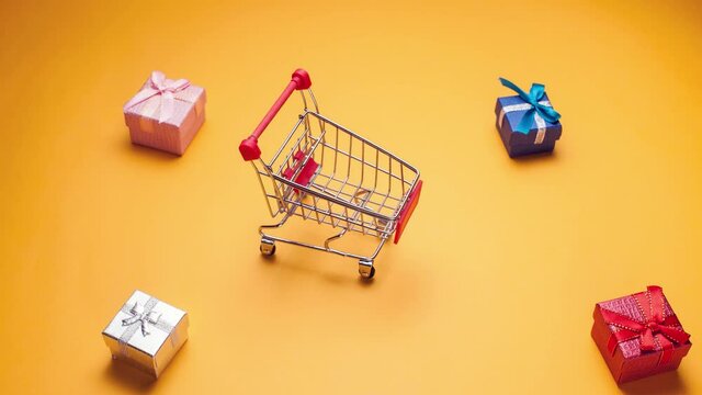 Shopping trolley moving from the left to the right side, loading with gift boxes and moving away on yellow background. Shopping concept. Stop motion footage