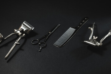 On a black surface are old barber tools. vintage manual hair clipper, comb, hairdressing scissors. black monochrome. black background. contrast shadows.  horizontal. optical illusion